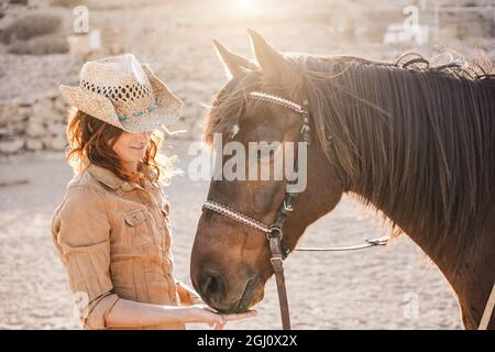 Giovane donna contadina che gioca con il suo cavallo al ranch fattoria - Focus su cappello donna Foto Stock