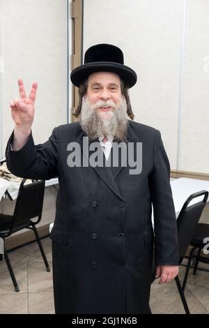 Un uomo ebreo ortodosso con lunghi margini ricci dà a questo fotografo un sorriso e un segno di pace. A Brooklyn, New York. Foto Stock