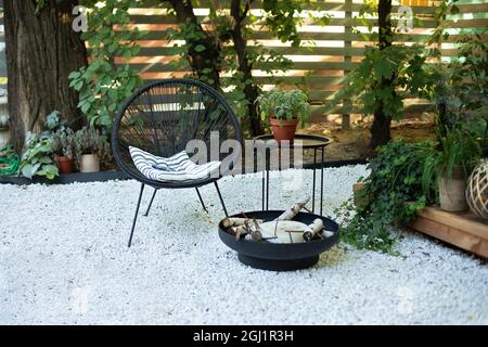 Veranda di casa con poltrona Acapulco, tavolino e pentole. Caminetto nero in metallo nel giardino sul patio sul retro. Patio all'aperto Foto Stock