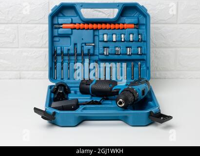 trapano portatile su una batteria in una valigetta di plastica aperta con accessori su un tavolo bianco Foto Stock