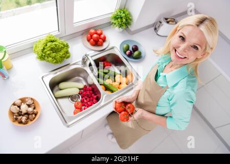 Vista dall'alto di una buona ragazza allegra sorridente nonna in grembiule lavando le verdure preparare la prima colazione a casa Foto Stock