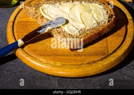 Fetta di pane rustico senza lievito naturale con lino, semi di papavero, semi di sesamo, miglio, zucca e semi di girasole, spalmato con burro, su un legno Foto Stock