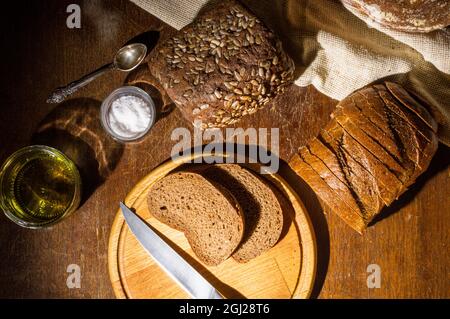 Still life - pane di grano saraceno senza lievito, vari tipi di pane nero, con olio d'oliva e sale grosso in vasi di vetro, un coltello e un tovagliolo di lino su un Foto Stock