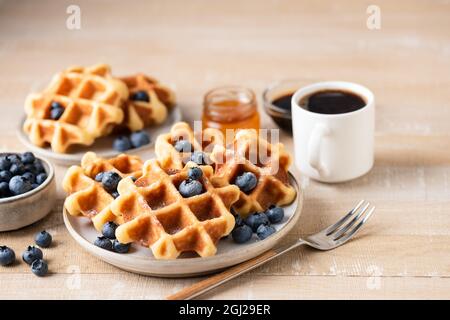 Waffle belgi con mirtilli e una tazza di caffè nero su tavola di legno, colazione in caffetteria Foto Stock