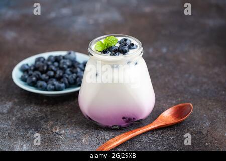 Yogurt al mirtillo in vaso su fondo tavola di cemento. Cibo sano, snack fitness dolce Foto Stock