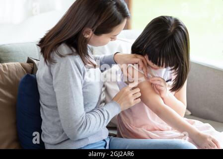 Madre asiatica che mette il bendaggio adesivo dell'intonaco di corte sulla sua figlia a casa Foto Stock