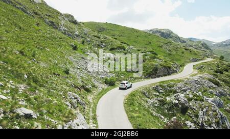 Una macchina bianca percorre la splendida strada verde di montagna del Montenegro. Antenna Foto Stock