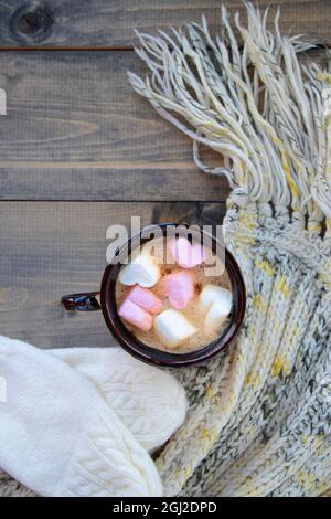 tazza con cioccolata calda e marshmallows a forma di cuore. bevanda calda su tavola di legno e sciarpa a maglia con guanti. fuoco morbido Foto Stock