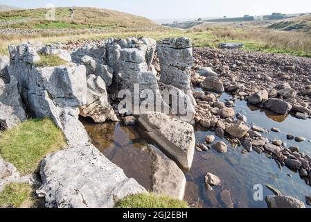 Winterscale beck è sotto le pendici di Whernside. Il becco era ad acqua molto bassa esponendo pilastri di pietra e un letto di macigno. Foto Stock