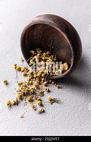 fuoco selettivo, tè in foglie verdi naturali. camomilla in ciotola di legno. angolo verticale, macro. su sfondo chiaro. per menu e caffè Foto Stock