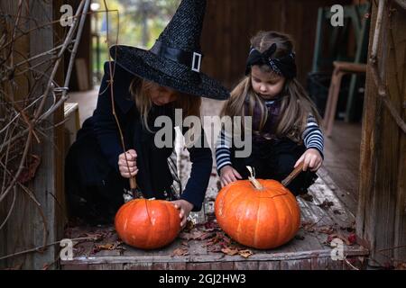 Le ragazze piccole fanno jack-o-lanterna dalle zucche grandi per la celebrazione di Halloween Holiday.Witch costume, cappello, cappotto. Tagliare con il coltello, estrarre la polpa con s. Foto Stock