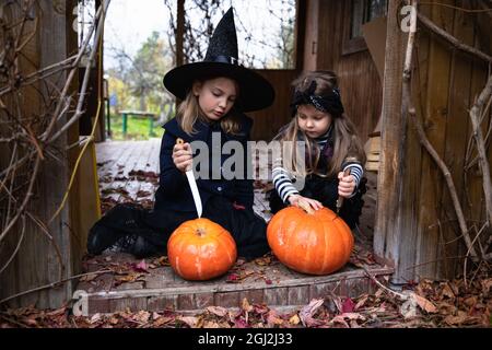 Le ragazze piccole fanno jack-o-lanterna dalle zucche grandi per la celebrazione di Halloween Holiday.Witch costume, cappello, cappotto. Tagliare con il coltello, estrarre la polpa con s. Foto Stock