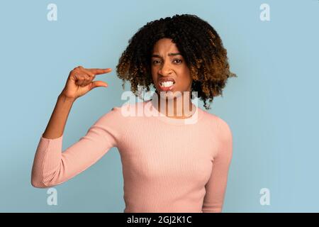 Dispiaciuta Black Woman misurando poco invisibile oggetto con le dita, delusa African American Female mostrando piccola quantità di qualcosa mentre St Foto Stock