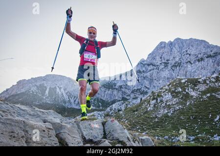 Ultra sentiero che corre in montagna. Un uomo alza le mani con i poli Foto Stock