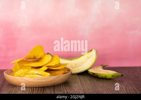 Banana chip o localmente noto come kerepek pisang in legno piatto con crudo metà banana. Punti di messa a fuoco selettivi. Sfondo sfocato Foto Stock