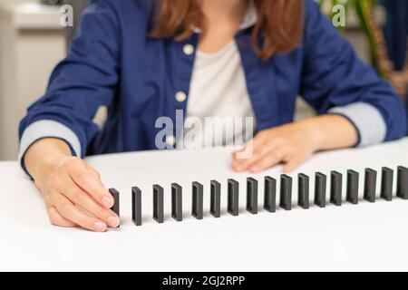 Una ragazza in una maglietta blu gioca a domino a casa su un tavolo bianco di legno. Messa a fuoco selettiva. Primo piano Foto Stock