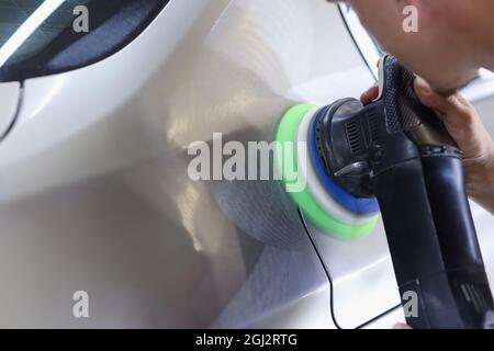 L'uomo tiene la lucidatrice in mano e lucida l'automobile. Servizi concetto di lavaggio auto Foto Stock