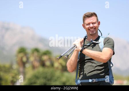 Uomo sorridente che tiene i bastoni scandinavi in cima al primo piano di montagna Foto Stock