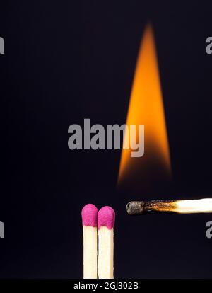 Primo piano di una partita bruciante vicino a fiammiferi freschi su sfondo viola scuro. Concetto di ispirazione. Foto Stock