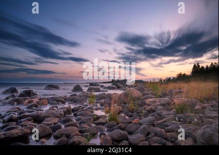 Lunga esposizione di un magnifico tramonto morbido e colorato vicino alla pietra del mare. Bel movimento nube con pietre di mare. Foto Stock