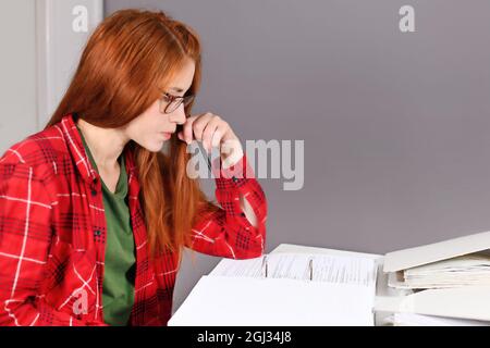 Donna con capelli rossi seduti alla scrivania guardando il documento nella lima ad anello Foto Stock