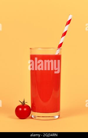 Bicchiere con succo di pomodoro rosso e cannuccia a strisce davanti allo sfondo giallo Foto Stock