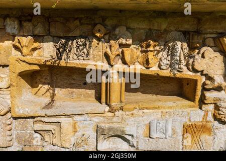 Frammenti della pietra intagliata dall'Abbazia di Hailes incastonati nel muro del cimitero della chiesa di San Pietro vicino a Stanway House, Cotswolds, Inghilterra Foto Stock