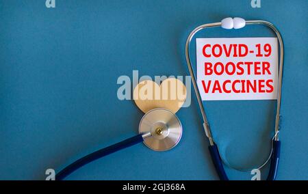 Covid-19 richiamo colpi vaccini simbolo. Carta bianca con le parole vaccini di richiamo Covid-19, sfondo blu bello, cuore di legno e stetoscopio. Covi Foto Stock