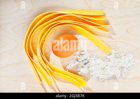 Grande pappardelle di pasta piatta all'uovo su sfondo ligneo con uova e farina Foto Stock
