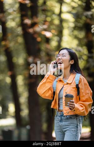 studente asiatico ridendo con occhi chiusi mentre parla sullo smartphone all'aperto Foto Stock
