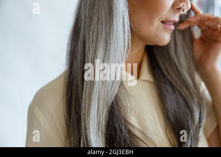 Donna di mezza età con bei capelli grigi pone su sfondo grigio chiaro Foto Stock