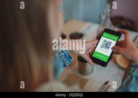 App per smartphone Woman checking con certificato di immunizzazione in ristorante. Lo stato è valido. Foto Stock