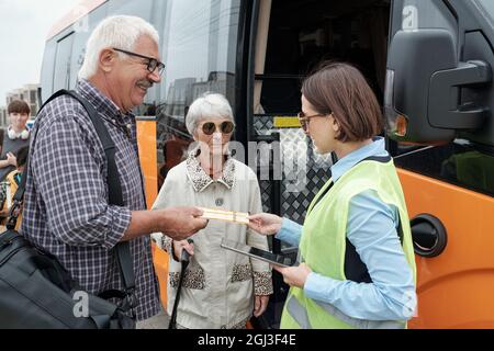 Coppia caucasica senior in piedi alla porta aperta dell'autobus e mostrando i biglietti per il supervisore dell'autobus con tablet Foto Stock
