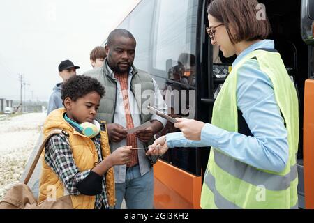 Grave padre e figlio afroamericano che mostra il biglietto per il supervisore del trasporto mentre si salire in autobus Foto Stock