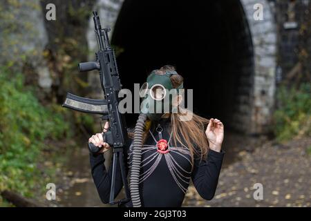 Una donna in abito nero e maschera a gas con una mitragliatrice nelle mani Foto Stock