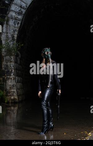 Una donna in abito nero e maschera a gas con una mitragliatrice nelle mani Foto Stock