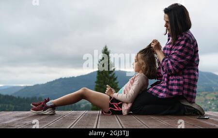 madre che brucia i capelli della figlia all'aperto mentre si siede sulla terrazza Foto Stock