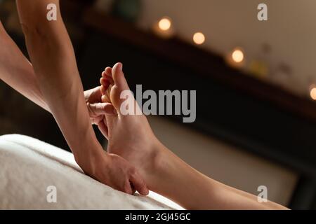 Massaggiatore che fa un massaggio ai piedi con candele sullo sfondo Foto Stock