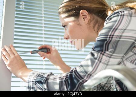 Donna installazione di persiane con cacciavite Foto Stock