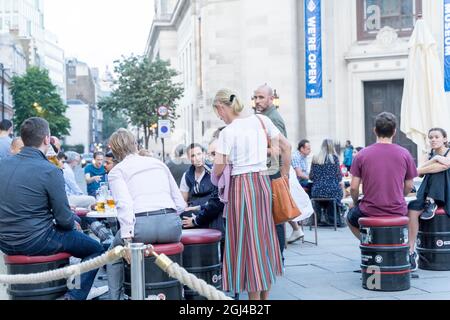 La gente gode del caldo clima autunnale in Covent Garden seduto fuori porta sul marciapiede zona salotto Londra Inghilterra Foto Stock