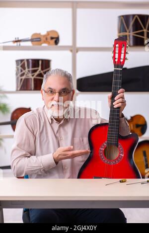 Vecchio riparatore che ripara gli strumenti musicali sul posto di lavoro Foto Stock