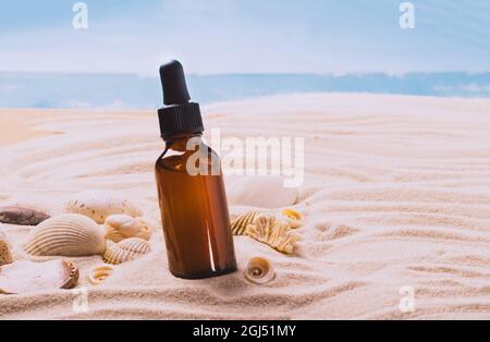 Bottiglia di vetro con olio essenziale siero prodotto cosmetico sfondo di spiaggia di conchiglie sabbia, presentazione del prodotto Foto Stock