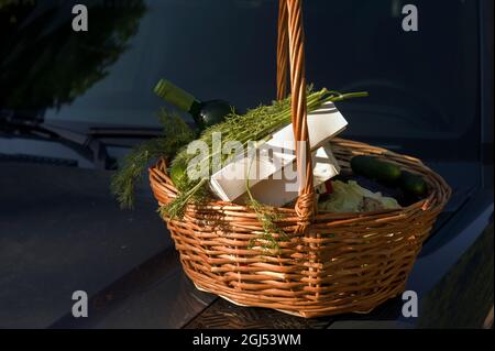 Un cestino di vimini per pic-nic con bevande e cibo su un cofano auto Foto Stock