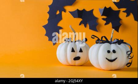 Due zucche bianche divertenti su uno sfondo arancione, Halloween vacanza, sullo sfondo nero pipistrelli fuoco sfocato, copia del testo Foto Stock