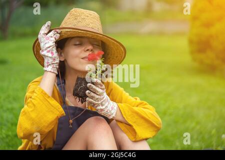 Una giovane donna giardiniere sta tenendo un fiore di petunia in una pentola di torba Foto Stock