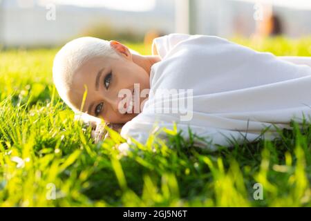 Ritratto di giovane sorridente donna europea a capelli corti che posa sul verde prato parco estivo. Bella ragazza bionda felice all'aperto. Foto Stock