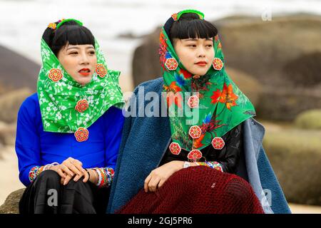 Cina, provincia di Fujian, Hui'an. Due giovani donne in abito tradizionale siedono al riparo dalle rocce. (Solo per uso editoriale) Foto Stock