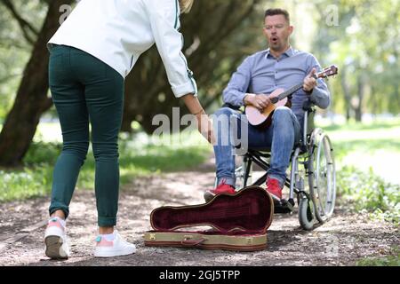 L'uomo disabili in sedia a rotelle suona la chitarra nei passanti del parco-da dare soldi. Foto Stock