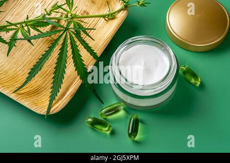 Crema viso anti-invecchiamento, pochi colpi di olio cbd e foglia di cannabis sativa su sfondo verde. Concetto di crema idratante per la canapa. Cura della pelle a base di erbe. Foto Stock