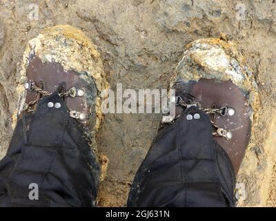 Scarponi da trekking sporchi dopo un'avventura fangosa. Stivali marroni su argilla fangosa marrone/grigia. Foto Stock